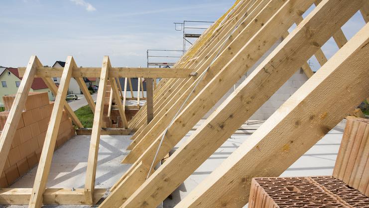 Blick auf eine Dachkonstruktion mit Holzsparren und Ziegelsteinen auf einer Baustelle unter blauem Himmel.