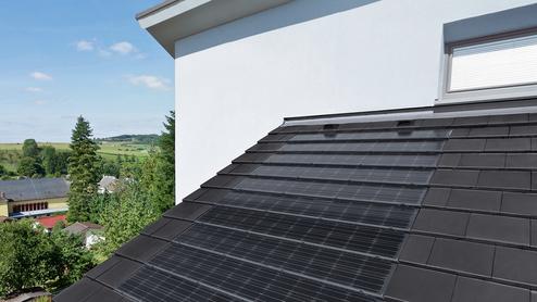 Dach mit schwarzen Solarpanelen über einer ländlichen Umgebung mit Häusern und Bäumen unter blauem Himmel.